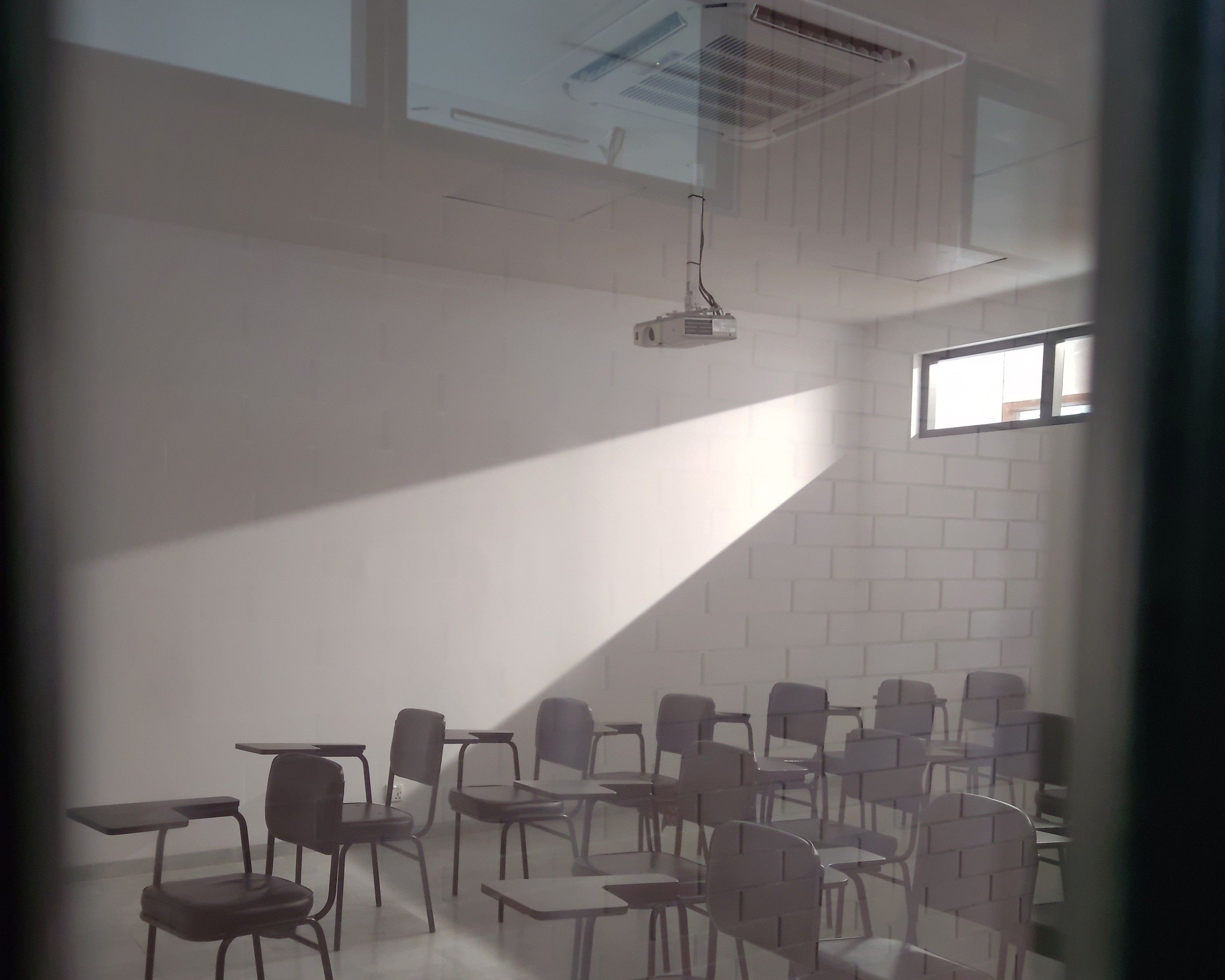 An empty classroom with rows of chairs, lit by a shaft of morning light across the wall