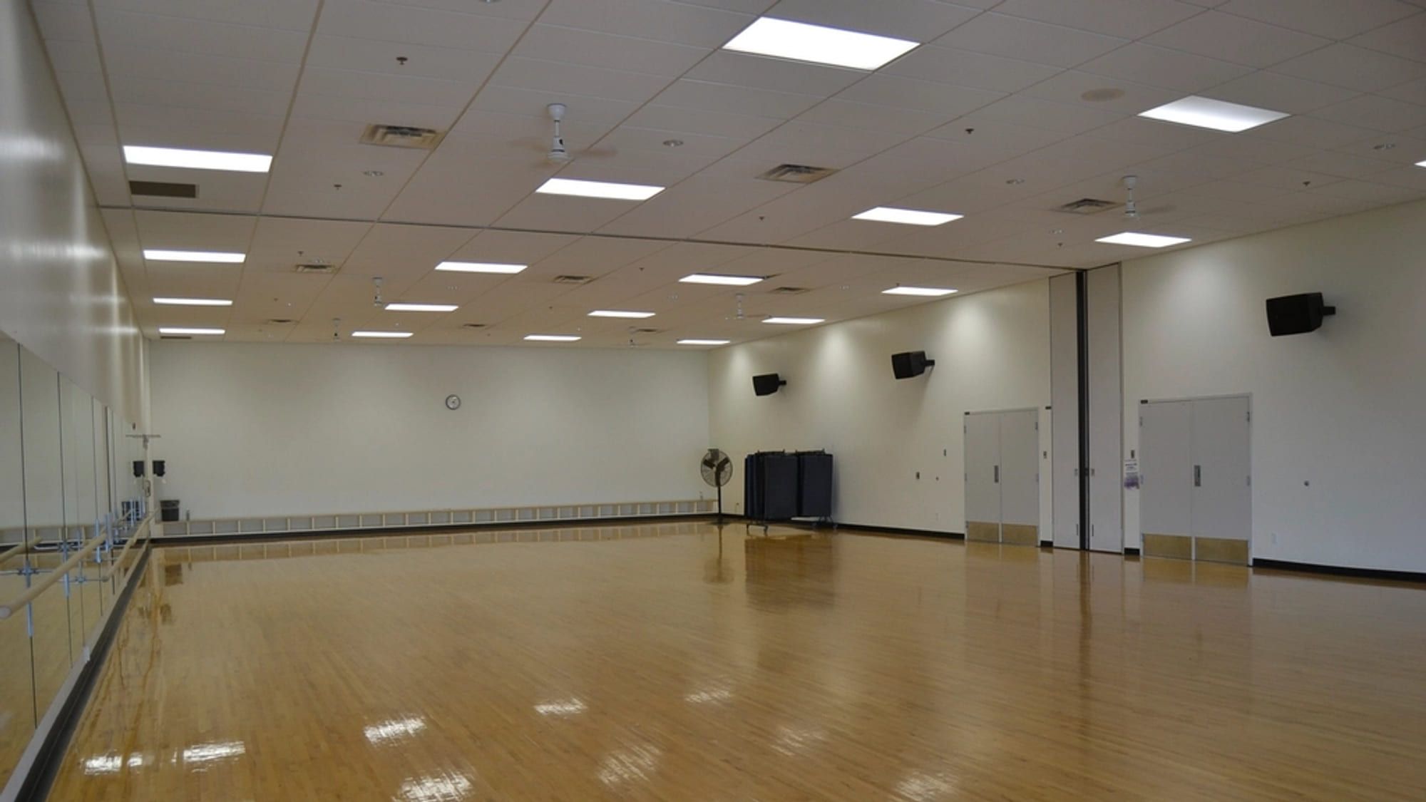 An empty mirrored studio with a wooden floor and a ballet barre