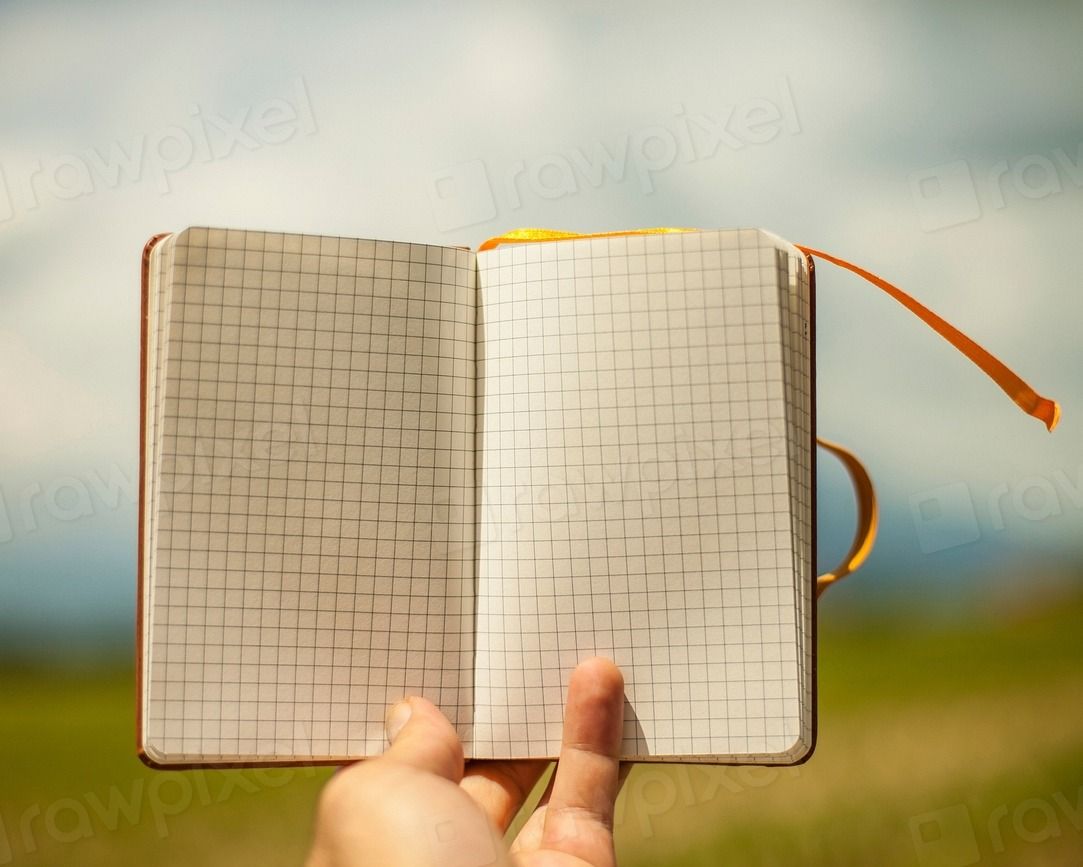A hand holding open a blank grid-paper notebook outdoors