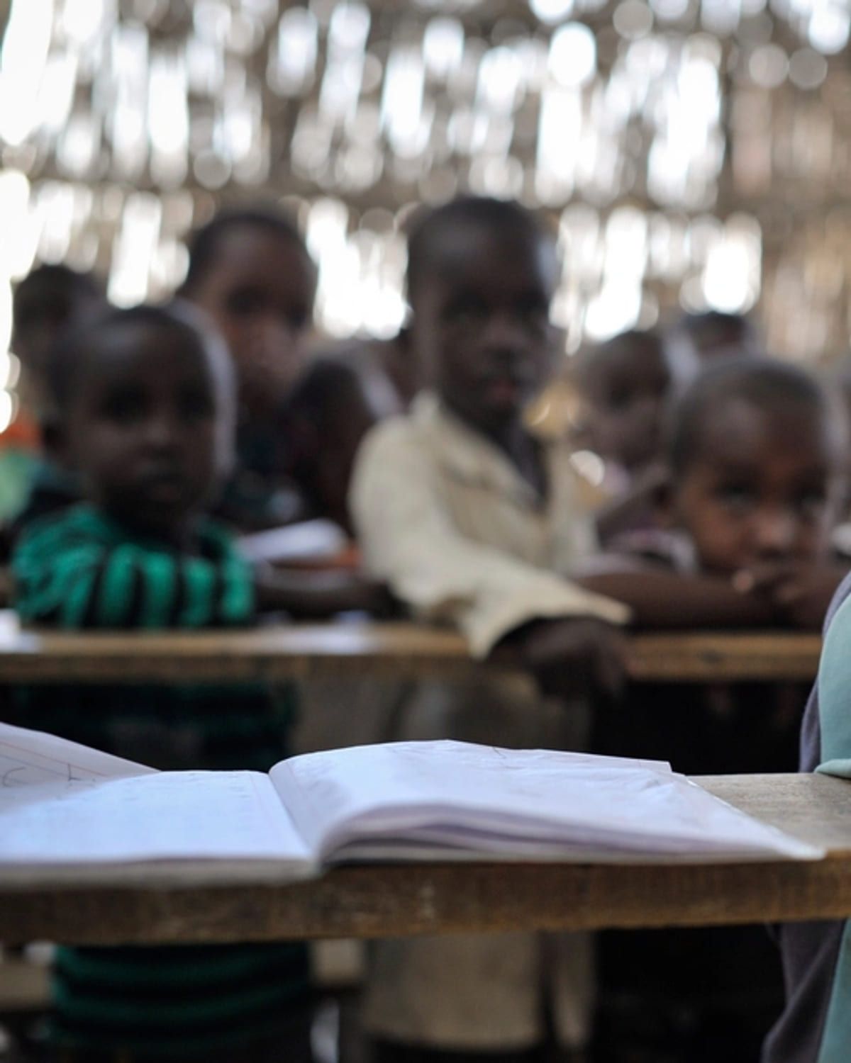 An open book on a desk, with a classroom out of focus behind it